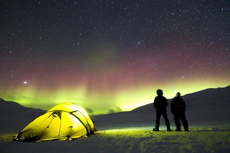 Two children standing by a yellow dome tent watching the Aurora Borealis